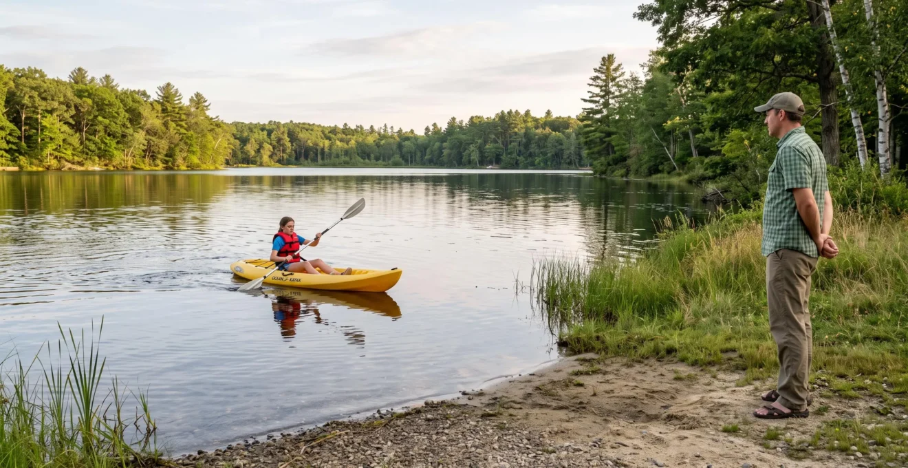 A beginner paddles a sit-on-top kayak across a small calm lake while an adult supervises from the shore.